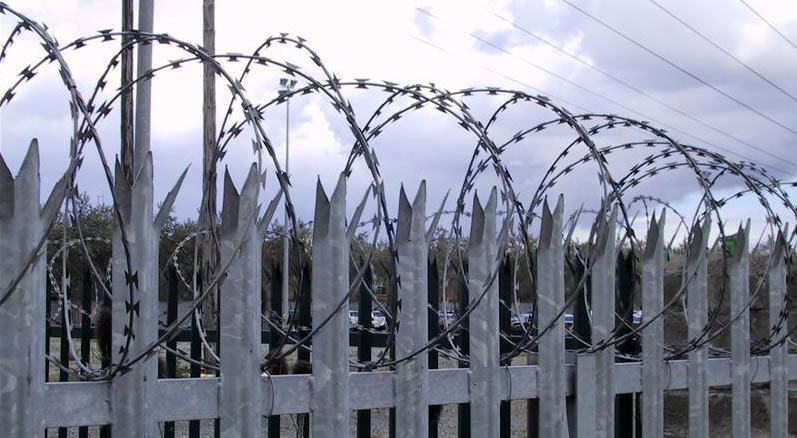 High-security steel palisade fencing with supporting rails and concertina wire above the perimeter