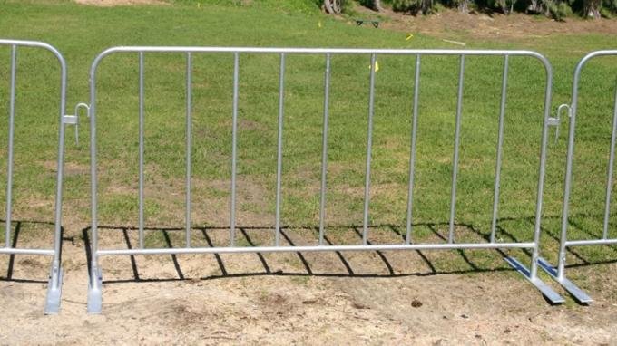 Three interlocked steel crowd control barriers standing on grass with flat metal feet